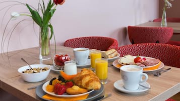 Uma mesa de café da manhã com pratos de comida, um croissant, morangos e um copo de suco de laranja.