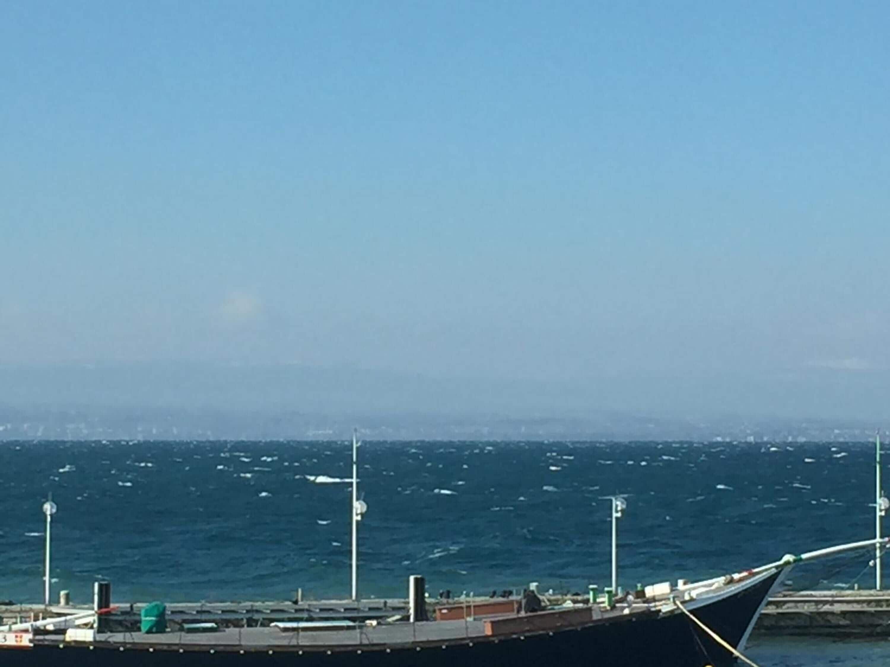 Un barco grande atracado en un muelle, con vista despejada al océano y al horizonte de la ciudad a lo lejos.