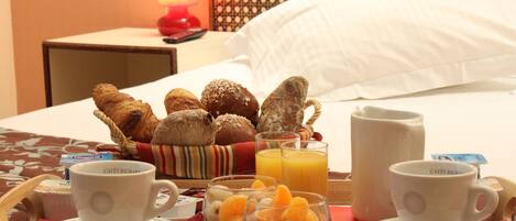 Un vassoio della colazione con croissant, succo d'arancia e tazzine di caffè su un letto d'albergo.