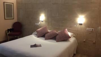 A hotel room with a bed, two wall-mounted lights, a red chair, and a framed picture on the wall.