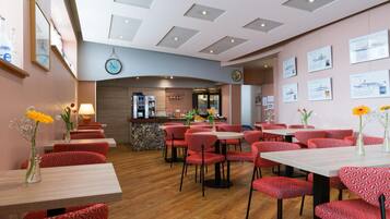 Een restaurant met rode gestreepte stoelen en tafels, een bar en informele posters aan de muur.