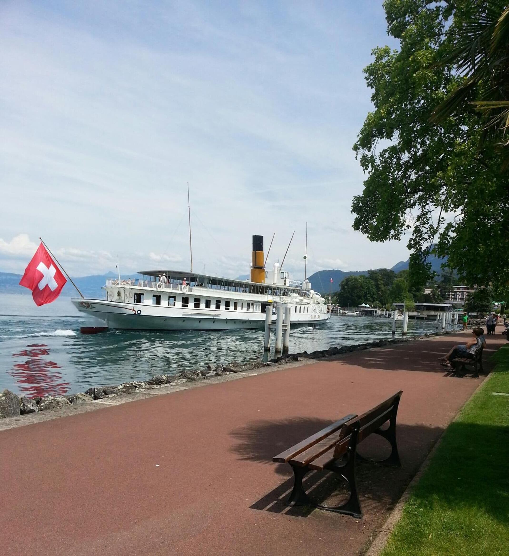 Un bateau était amarré à un quai, où flottait un drapeau rouge. Un chemin pavé et un banc se trouvaient également sur le quai.