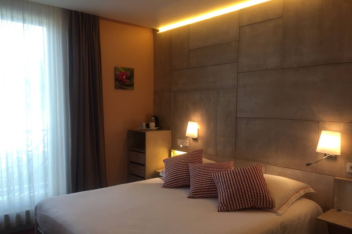 A hotel room with a large bed, two bedside lamps, a nightstand, and a wardrobe.