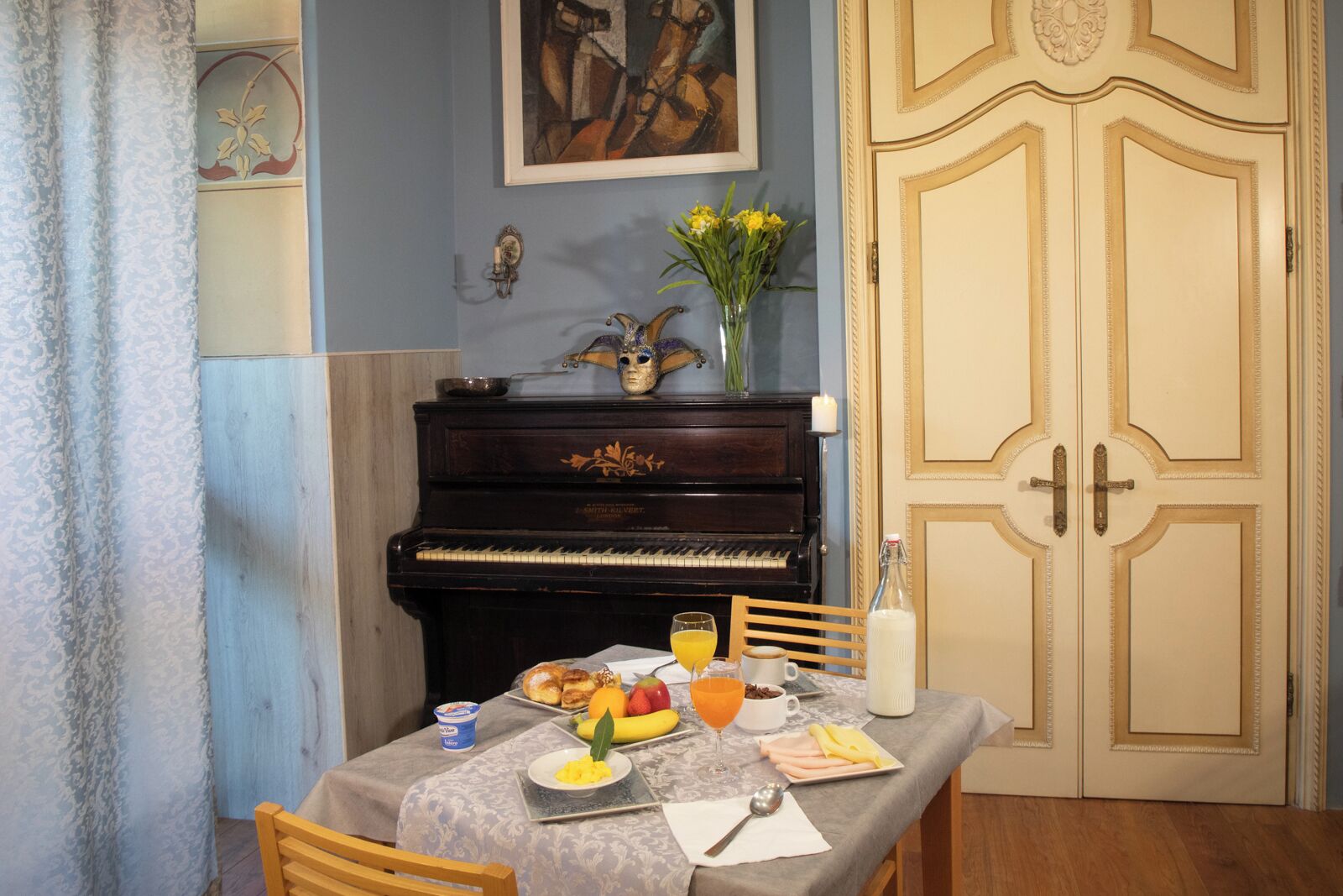 Un comedor con un piano, una mesa dispuesta para el desayuno y una puerta con paneles decorativos.