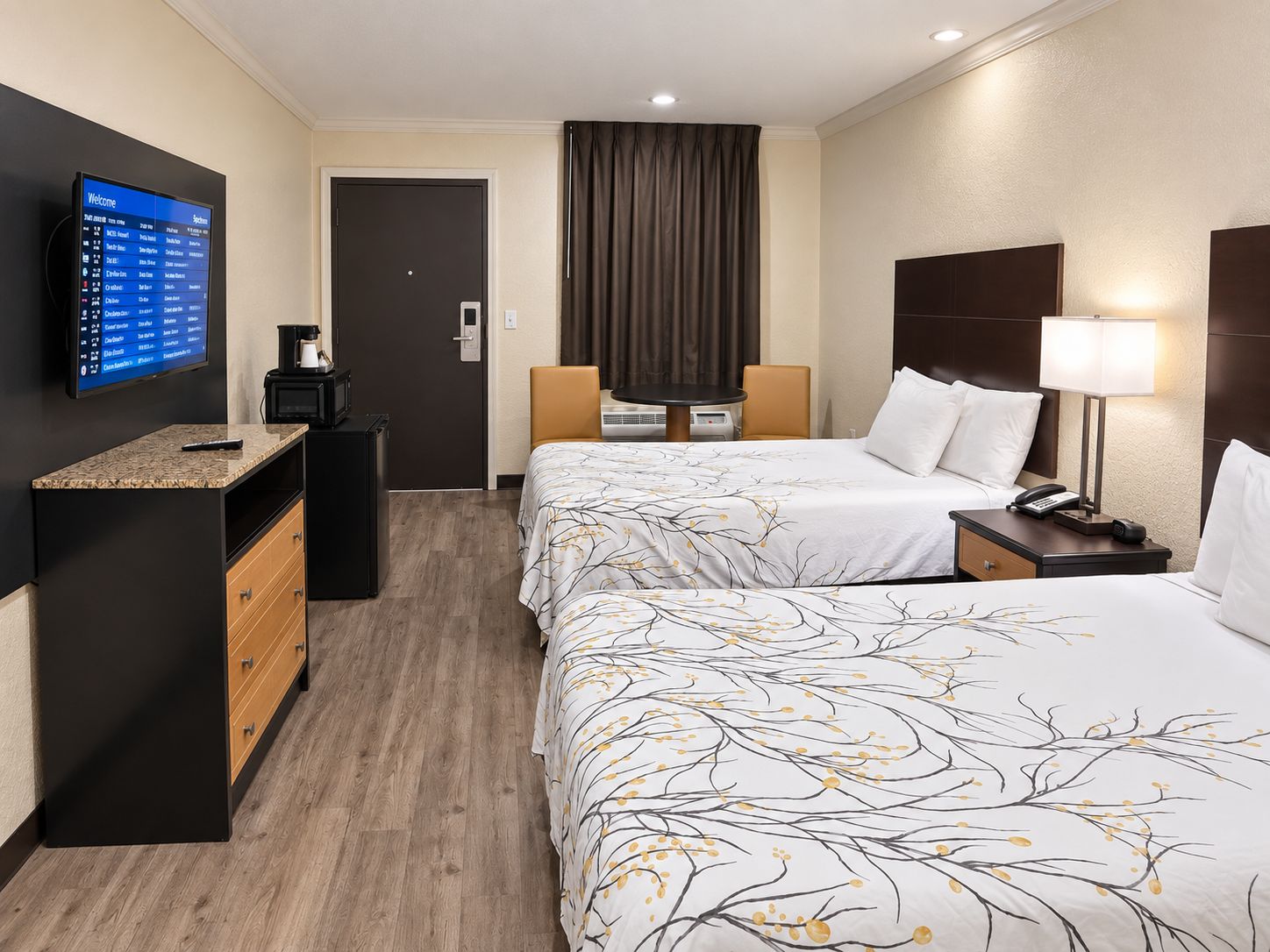 A hotel room with a bed, bedside table, lamp, TV, and a desk with drawers.