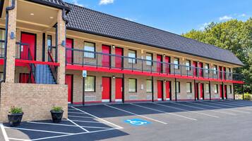 A multi-story motel with red doors and balconies, a parking lot with handicapped parking, and brick walls.