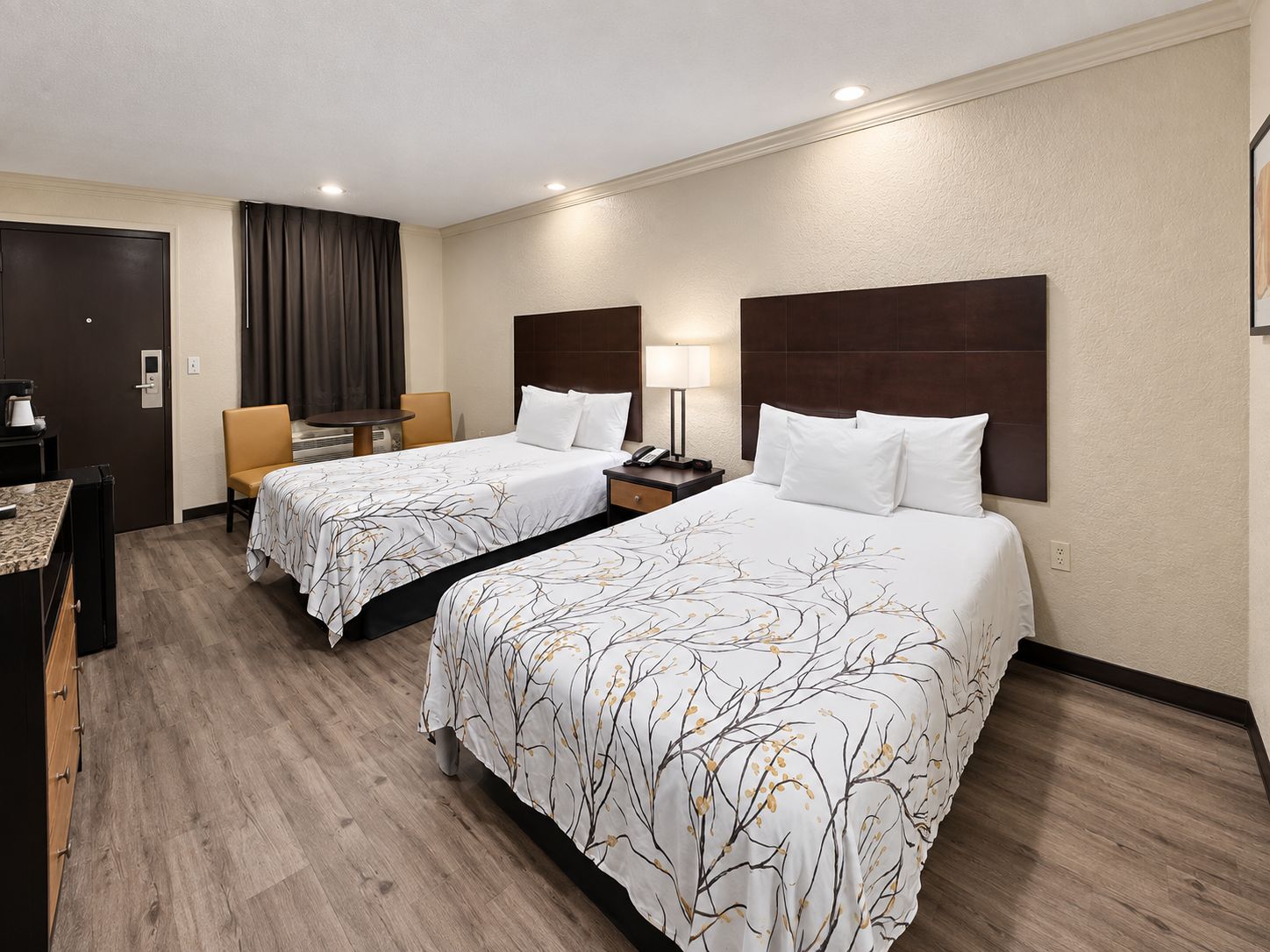A hotel room with two beds, a desk, a chair, a lamp, and a wardrobe.