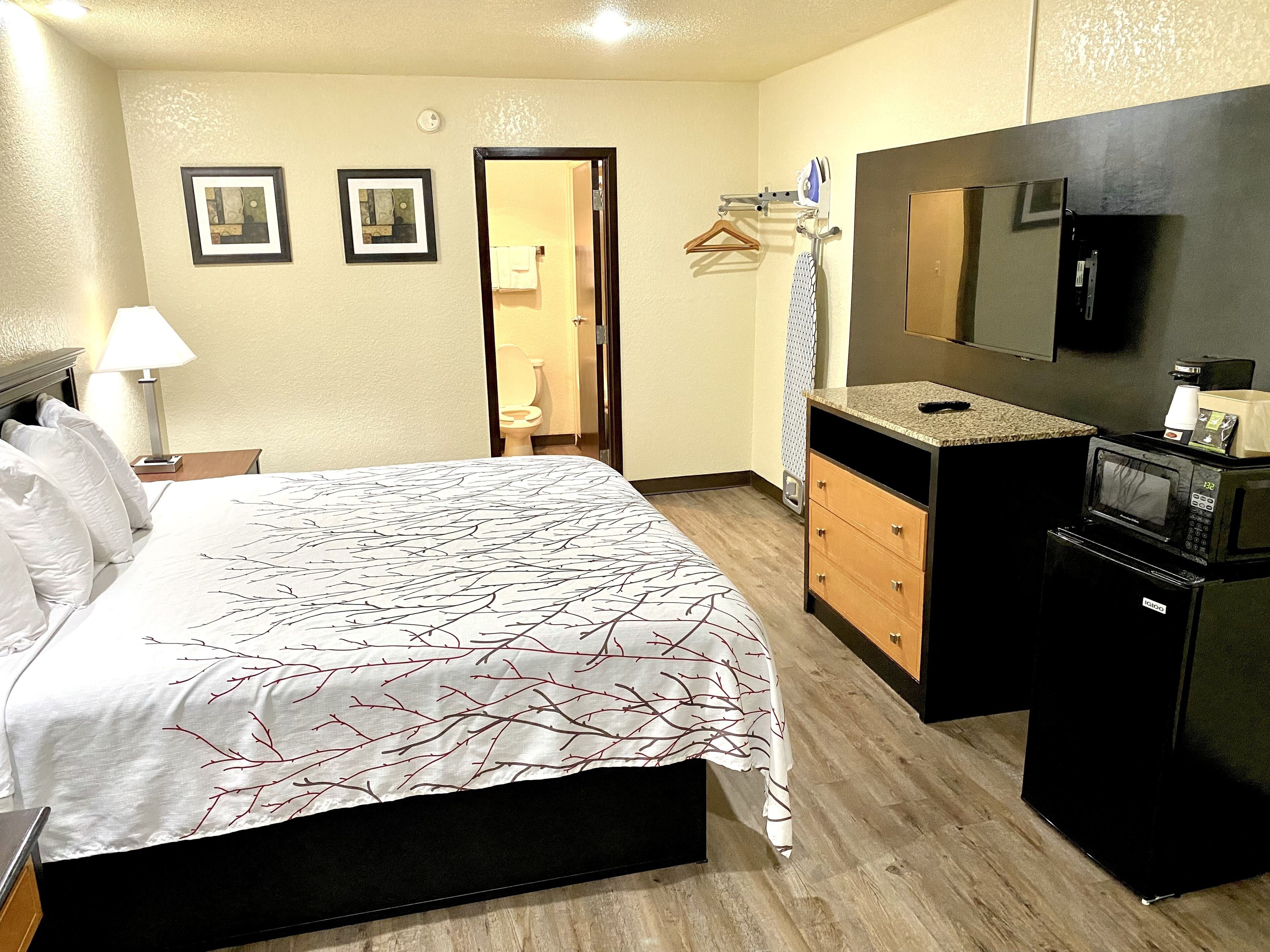 Habitación de hotel con cama, cómoda, microondas, televisor y puerta que da a un baño.