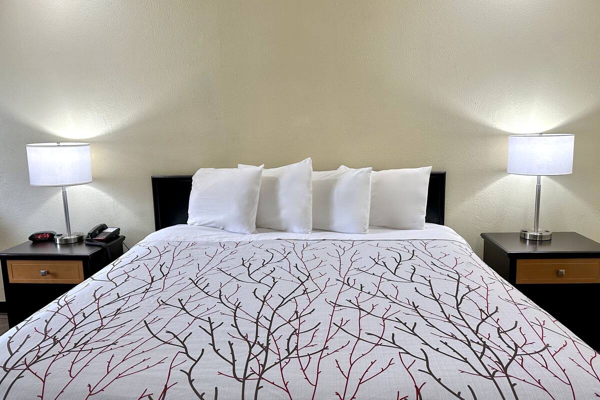 A hotel room with a bed, two bedside tables, a nightstand, a lamp, a clock, and a phone.