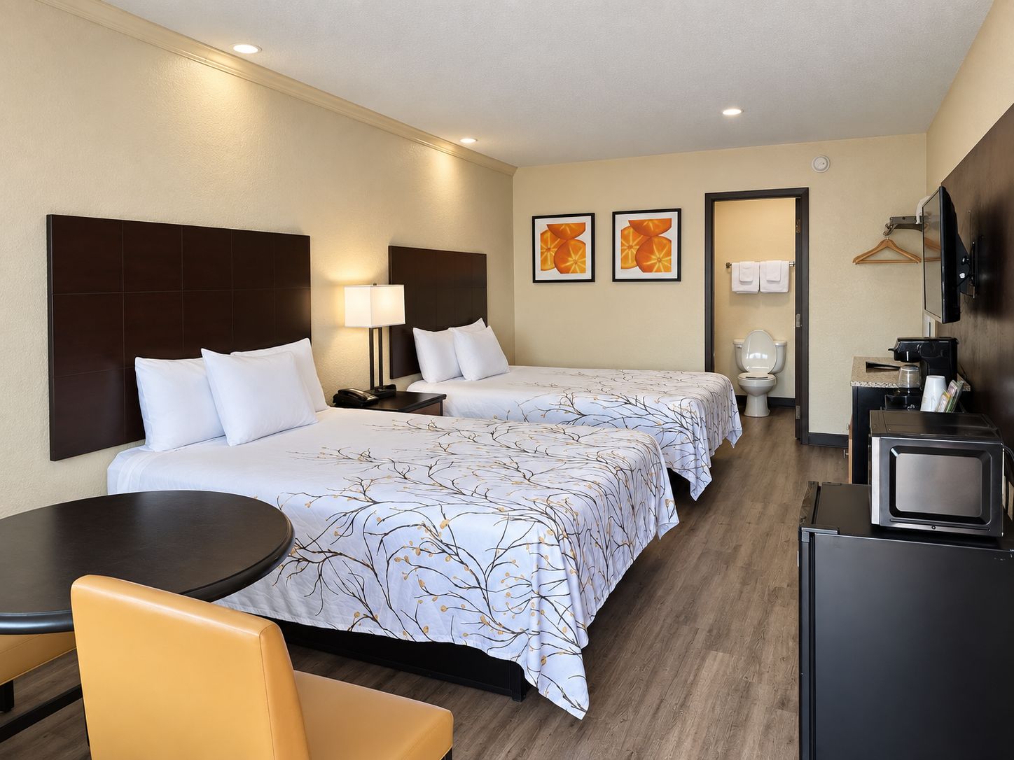 A hotel room with two beds, a desk, a chair, a TV, and a bathroom.