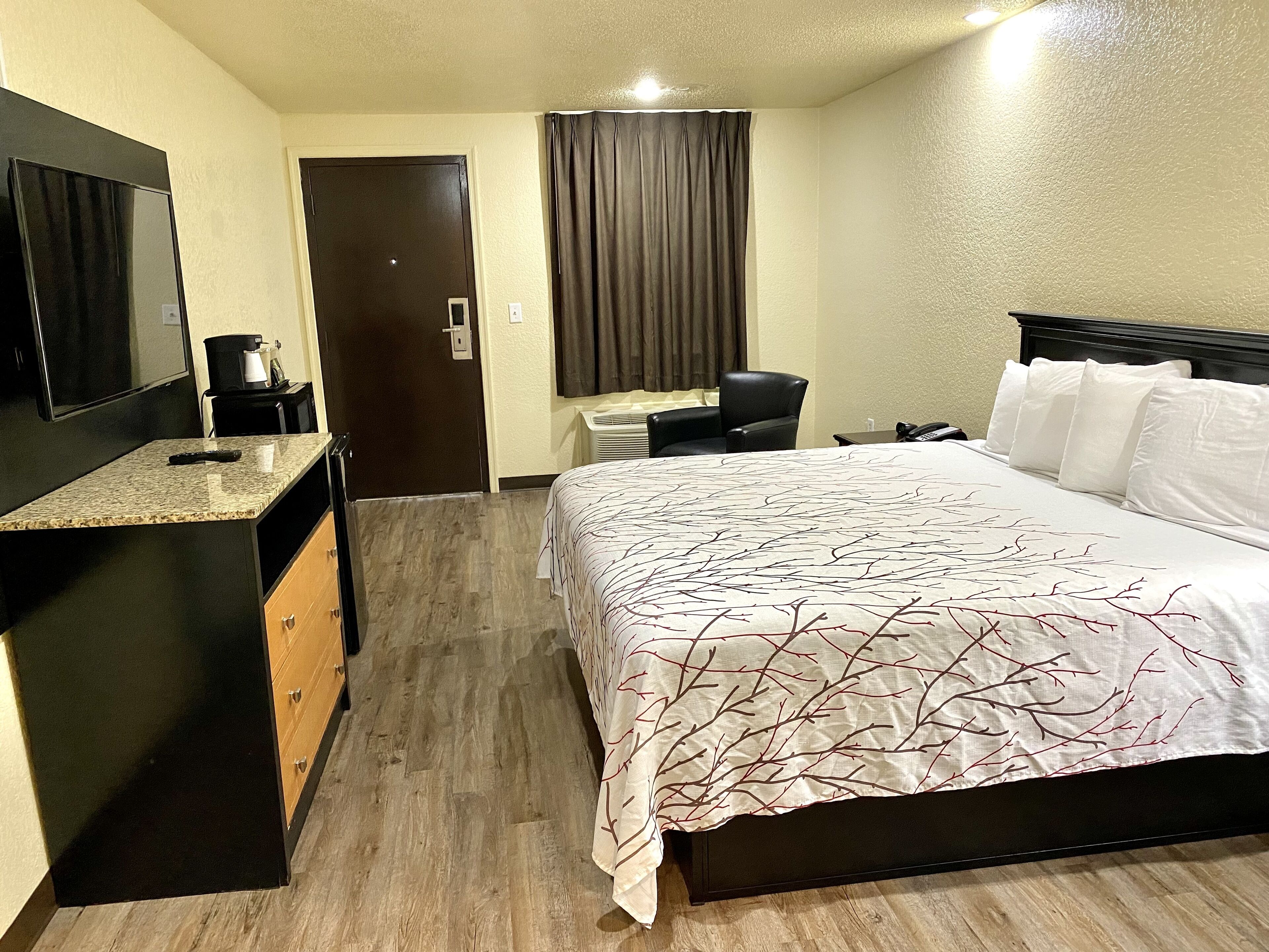 A hotel room with a bed, a desk, a chair, a coffee maker, and a TV.