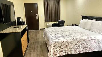 A hotel room with a bed, a desk, a chair, a coffee maker, and a TV.