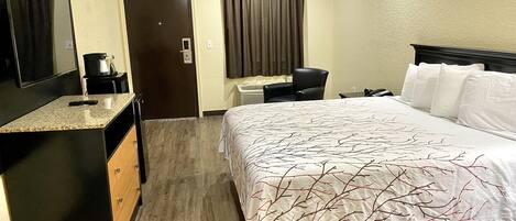 Habitación de hotel con cama, escritorio, silla, cafetera y televisor.
