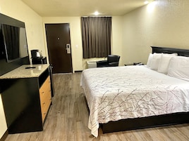 Quarto de hotel com cama, escrivaninha, cadeira, cafeteira e televisão.