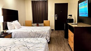 A hotel room with two beds, a desk with a TV, and a door.