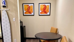 A small dining area with a round table and two chairs, a microwave, and a wall-mounted ironing board.
