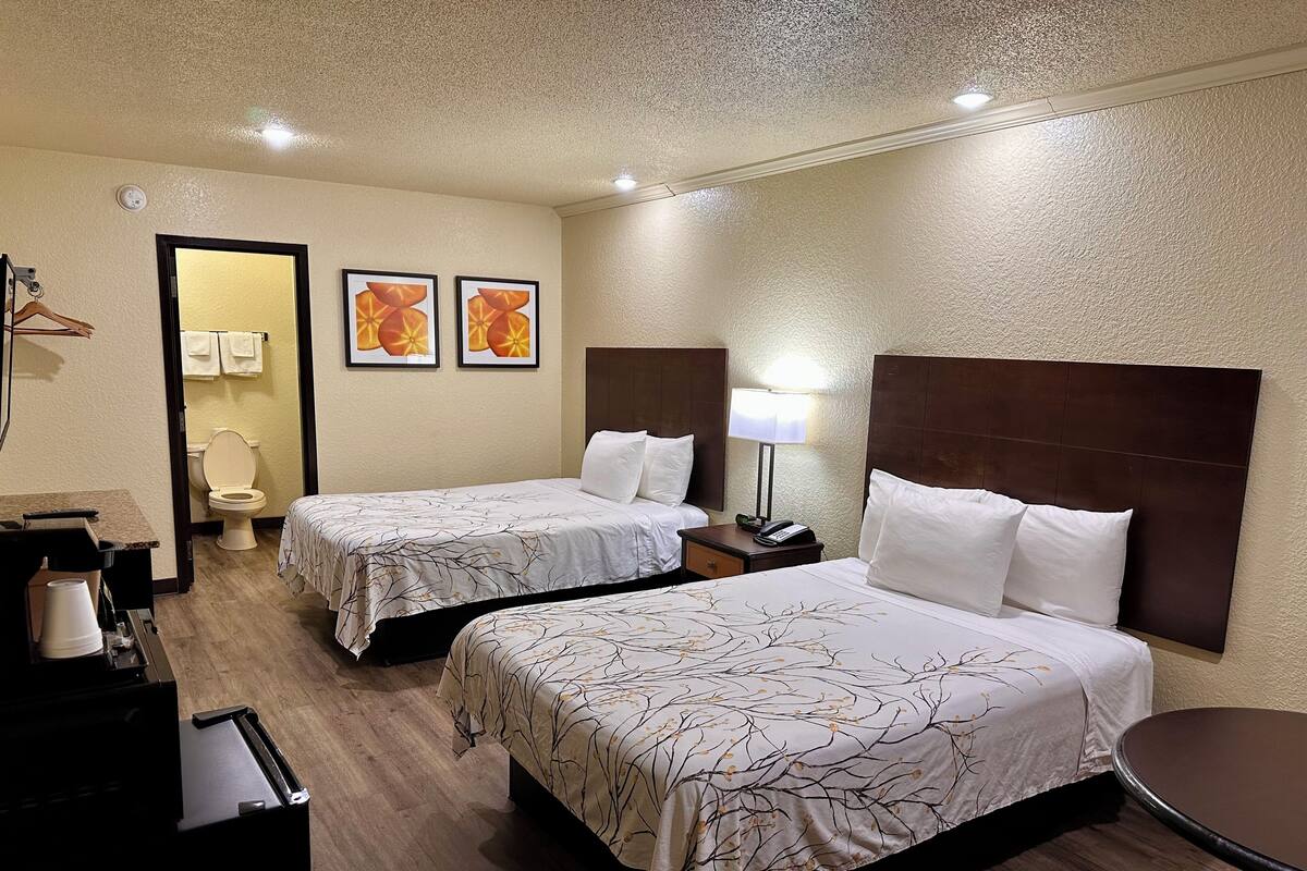 A hotel room with two beds, a bathroom, and a small table.