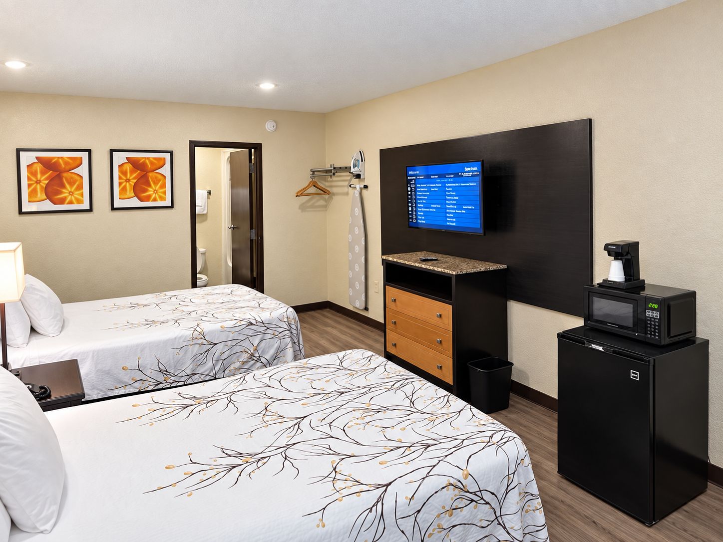 A hotel room with two beds, a television, a coffee machine, and a minibar.