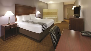 A hotel room with a large bed, two bedside lamps, a desk with a telephone, a television, and a bathroom with a bathtub and shower.