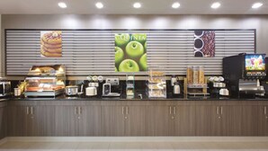 A self-service breakfast station with a variety of food items, a coffee machine, and a digital screen displaying a game.