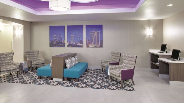 A modern lobby with a blue sofa, patterned chairs, a reception desk, and cityscape artwork on the wall.
