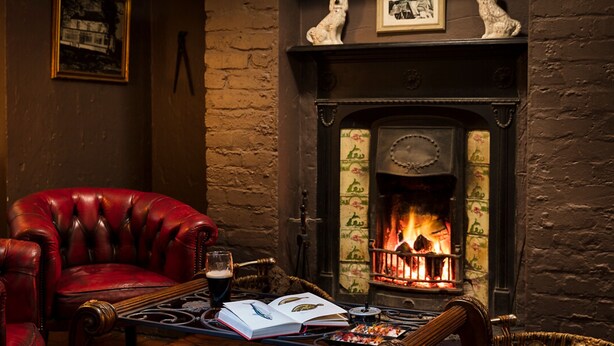 A leather armchair, a table with a book and a glass of beer, and a fireplace with a fire. - Brown Trout Golf & Country Inn (Coleraine)