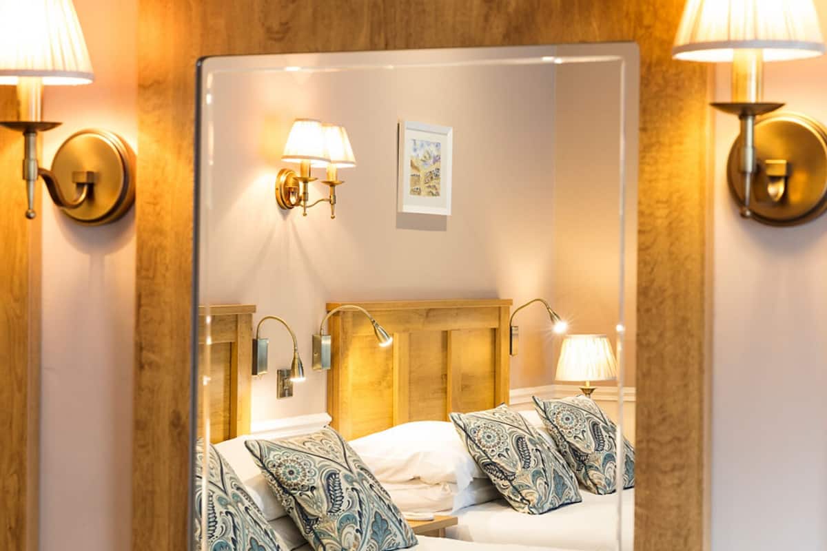 A hotel room with a large mirror, wooden headboard, and bedside lamps.