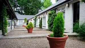 A covered walkway with potted plants and a building with white walls and black shutters. - Brown Trout Golf & Country Inn (Coleraine)