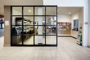 A modern retail store with a glass partition, a coffee machine, and various products on shelves.