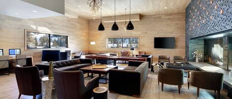 A modern hotel lobby with wooden walls, a large sofa, multiple chairs, a coffee table, and pendant lighting.