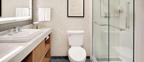 Un baño moderno con un espejo grande, un inodoro blanco, una cabina de ducha con paredes de vidrio y un tocador de madera.