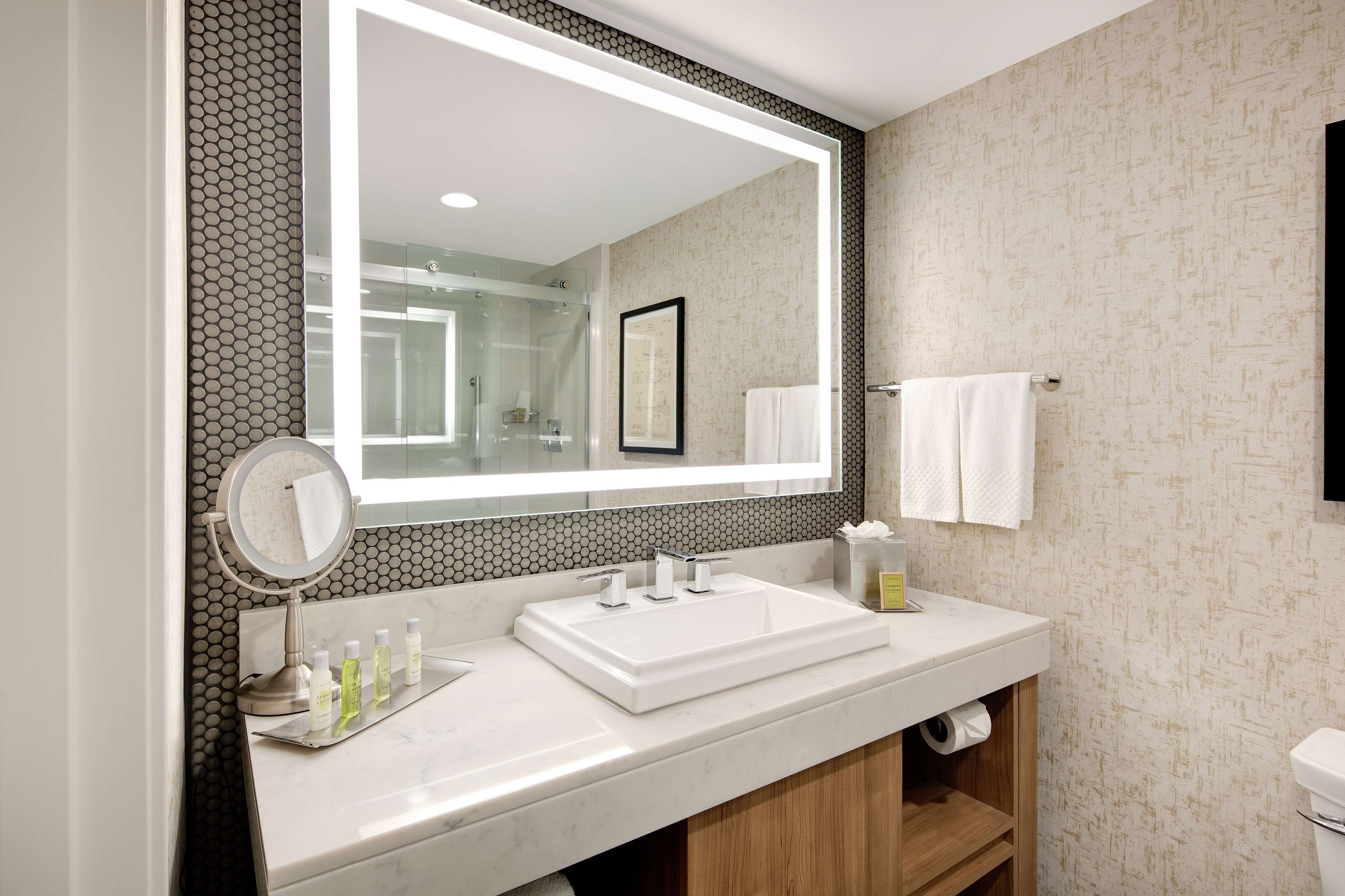A modern bathroom with a large mirror, a white sink, and a wooden vanity.