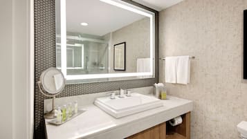 A modern bathroom with a large mirror, a white sink, and a wooden vanity.