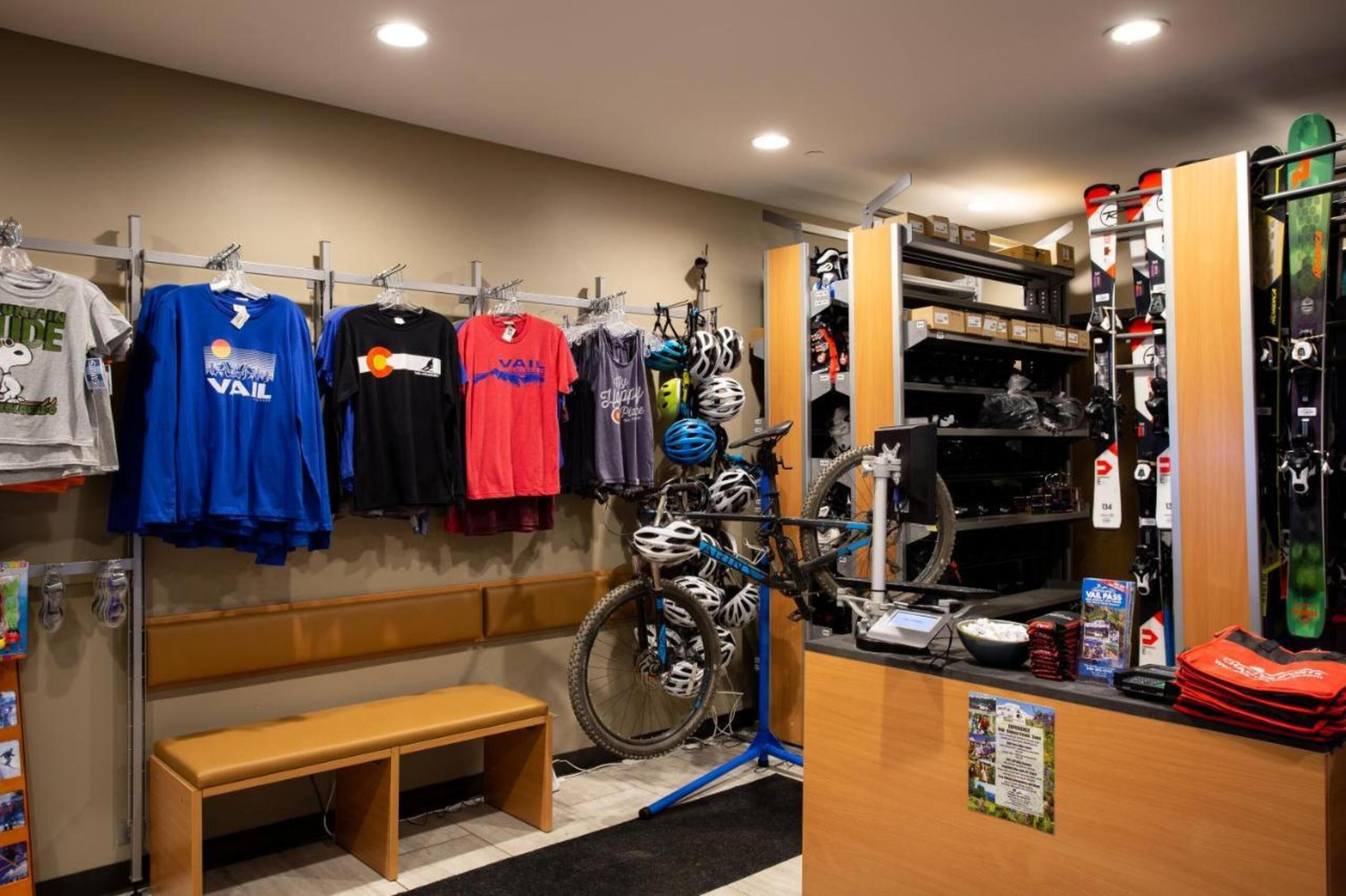 A room with a bench, a rack of cycling jerseys, helmets, and a bike.