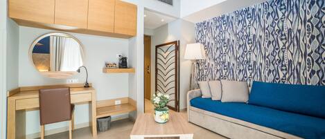A modern living room with a wooden desk, a round mirror, a blue sofa, and a patterned wall.