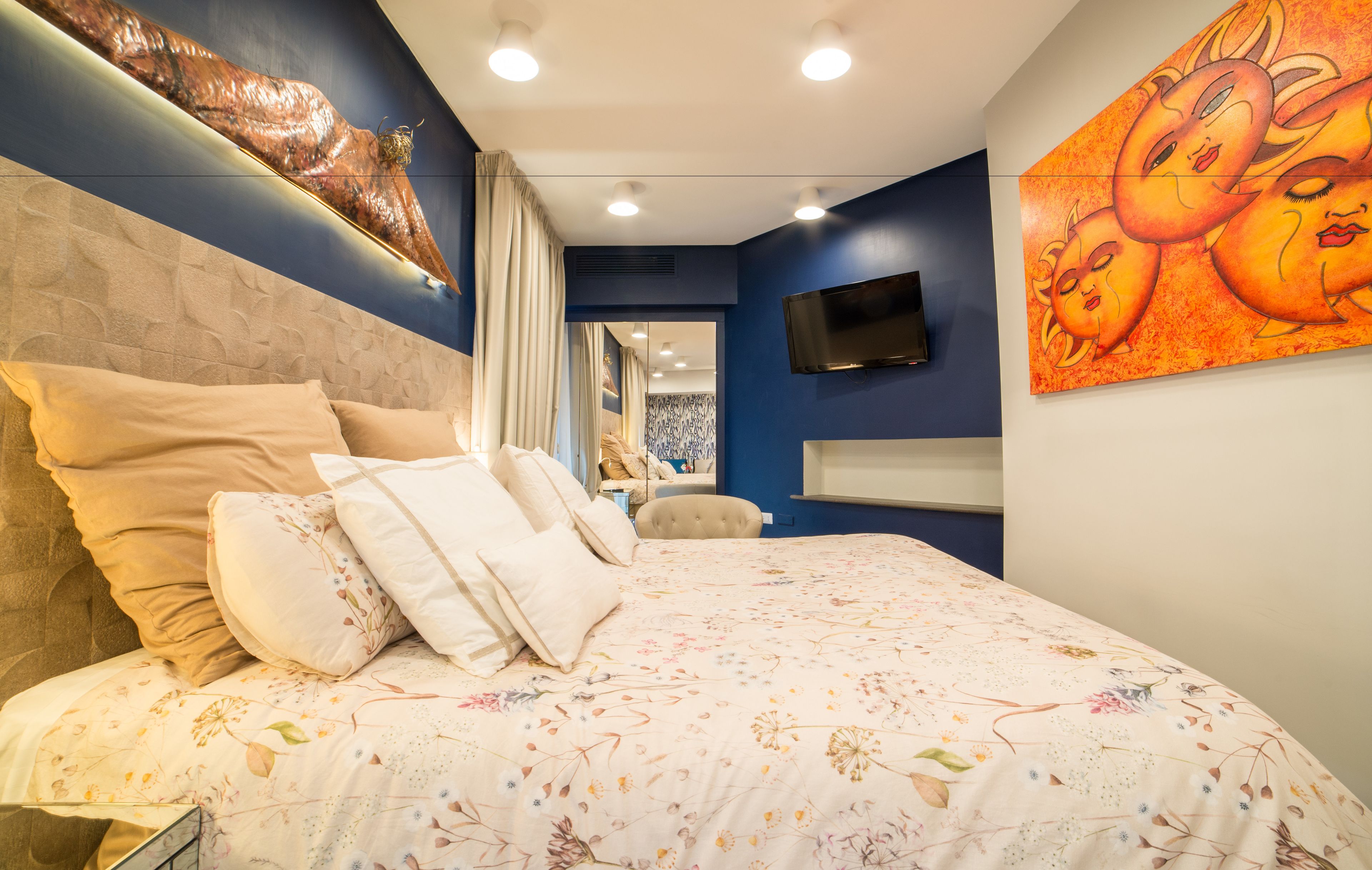 Une chambre dotée d’un grand lit, d’un téléviseur à écran plat fixé au mur et d’une œuvre d’art murale originale.