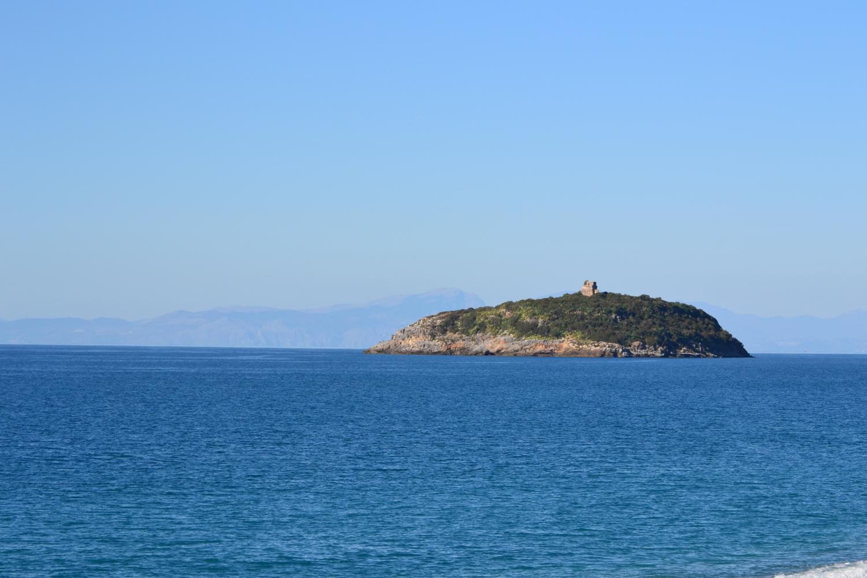 Eine kleine Insel mit einem Gebäude auf dem Gipfel, umgeben von ruhigem, blauem Wasser und fernen Bergen.