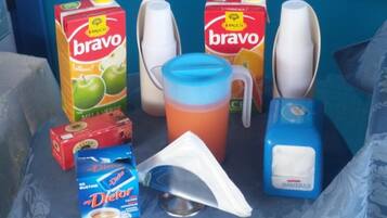 Ein Tisch mit einer blauen Tischdecke, zwei Kartons 'bravo'-Saft, eine weiße Tasse, eine blaue Wasserflasche, ein weißes Servietttuch und eine blaue Schachtel 'Dietor'-Energieriegel.