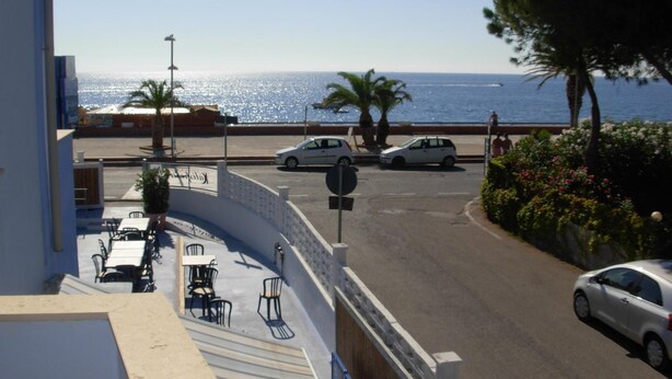 A coastal view from a balcony with outdoor seating, a street with parked cars, and a clear view of the sea. - Beach Hotel (Diamante)