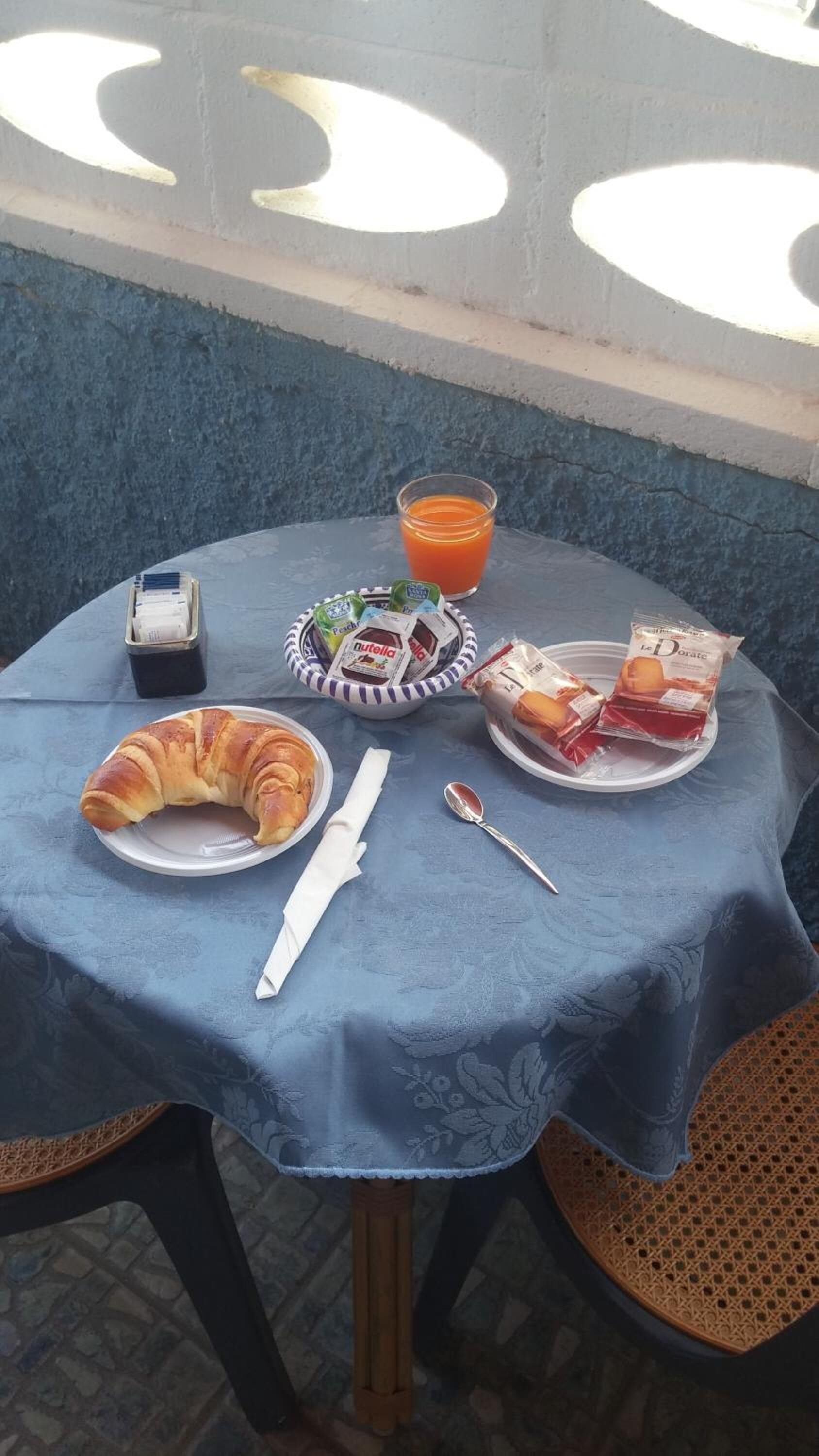 A table set with a croissant, a bowl of Nutella, a glass of orange juice, and a plate of bread.