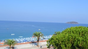 A beach with umbrellas and palm trees, a clear blue sky, and a distant island. - Beach Hotel (Diamante)