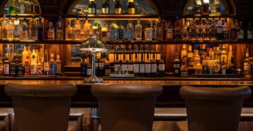 Un bar con taburetes de cuero y una variedad de botellas de licor.