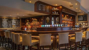 A bar area with a selection of cocktails, wine, and spirits. There are bar stools and a bar counter with a selection of bottles and a beer tap.