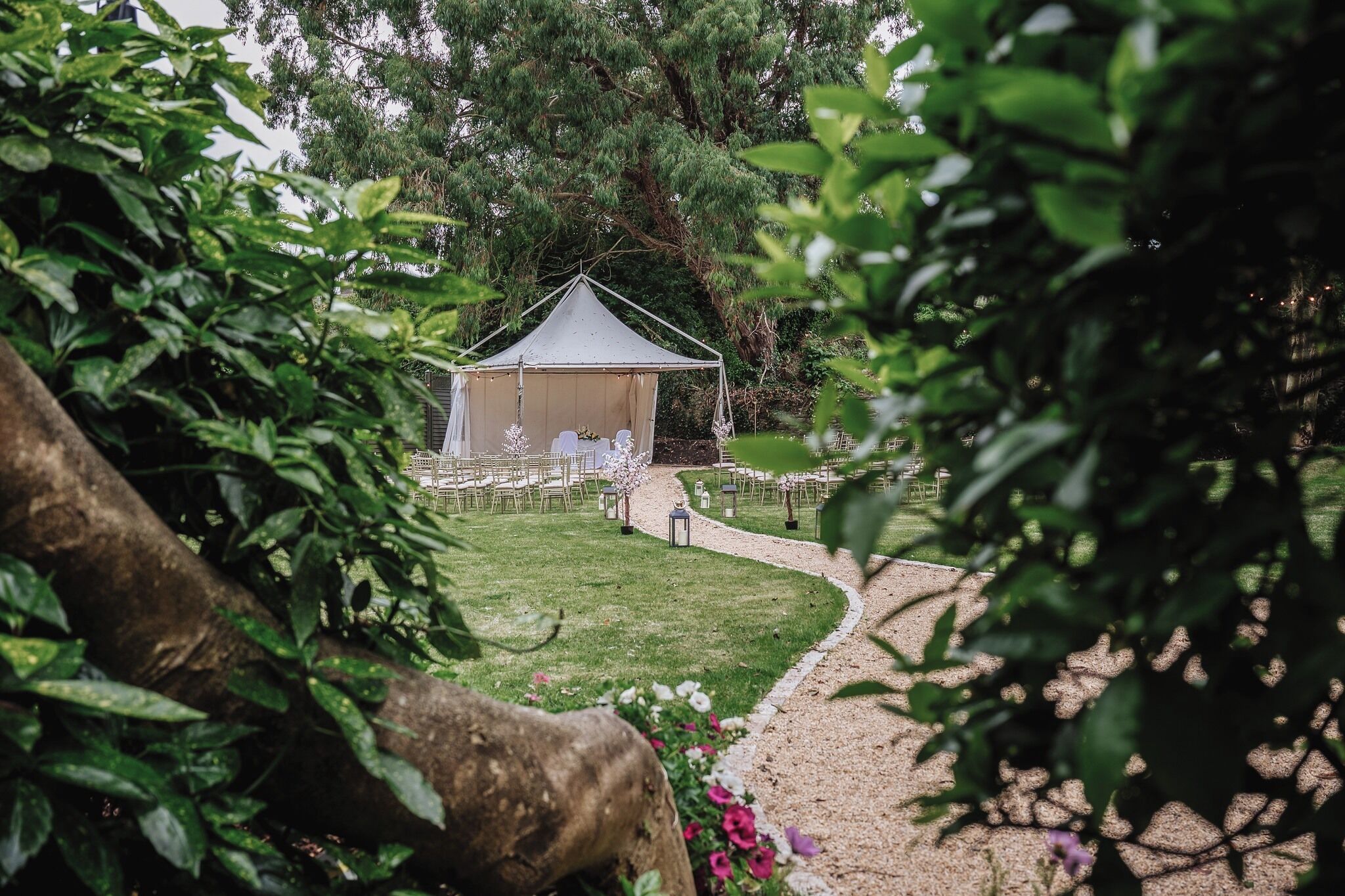 A tented wedding venue with a gravel path leading to it, surrounded by greenery.