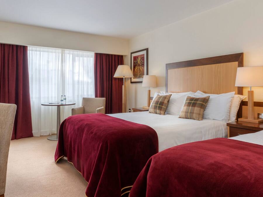 A hotel room with two beds, a desk, a chair, a small table, and a window with curtains.