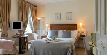 Una habitación de hotel con una cama, lámparas de noche, televisión, escritorio con lámpara y una silla.