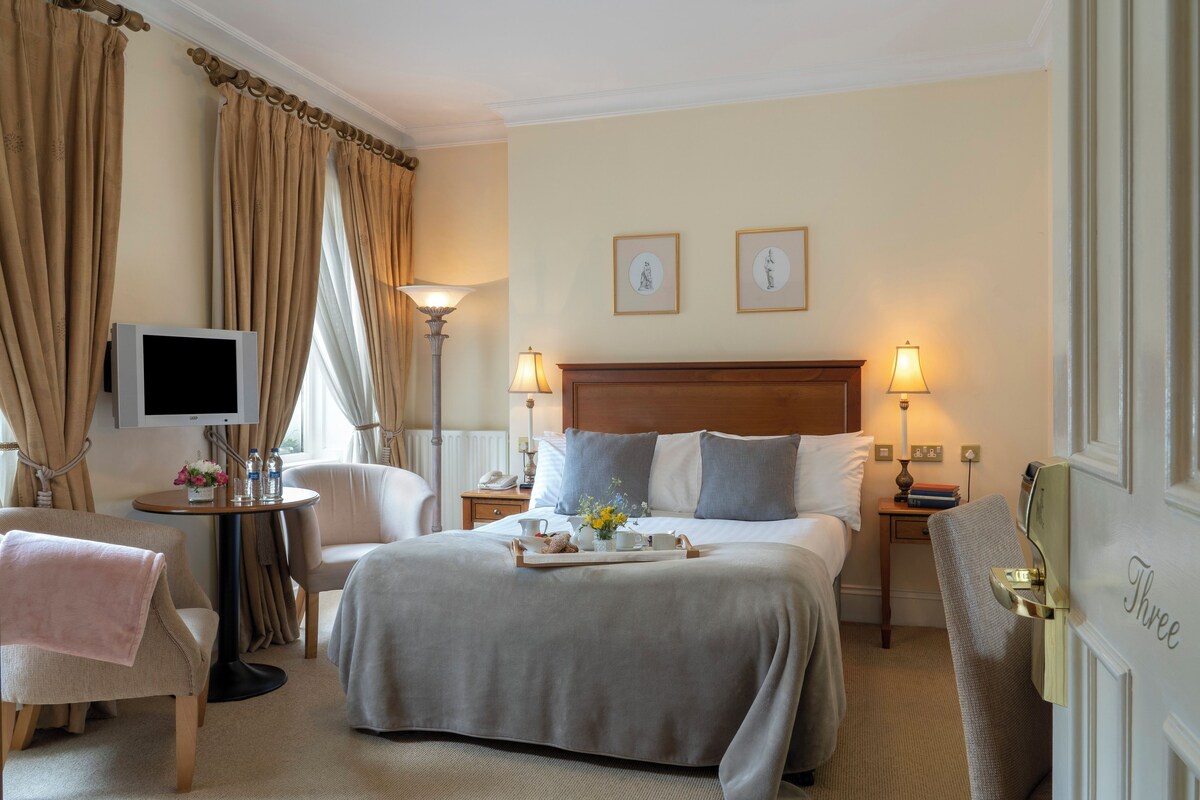 A hotel room with a large bed, a bedside table, a chair, a television, and a lamp.