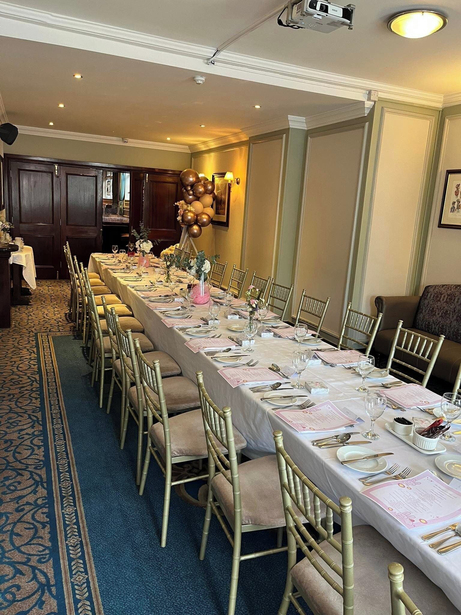Una larga mesa de banquete dispuesta para un evento formal, con sillas, vajilla y un arreglo decorativo de globos.