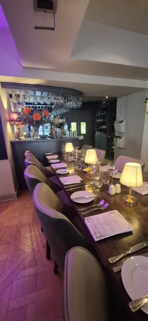 A dining area with a long table set for a meal, chairs, and a bar area in the background.
