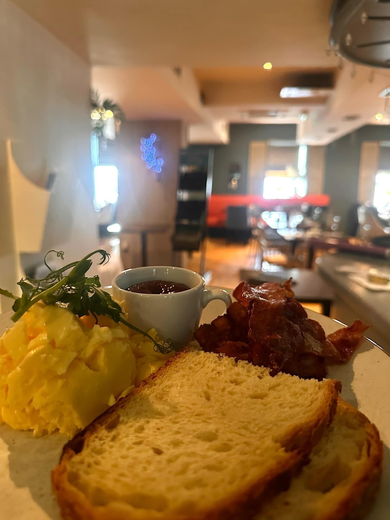 Un plato de desayuno con huevos, tostadas, tocino y una taza de café.